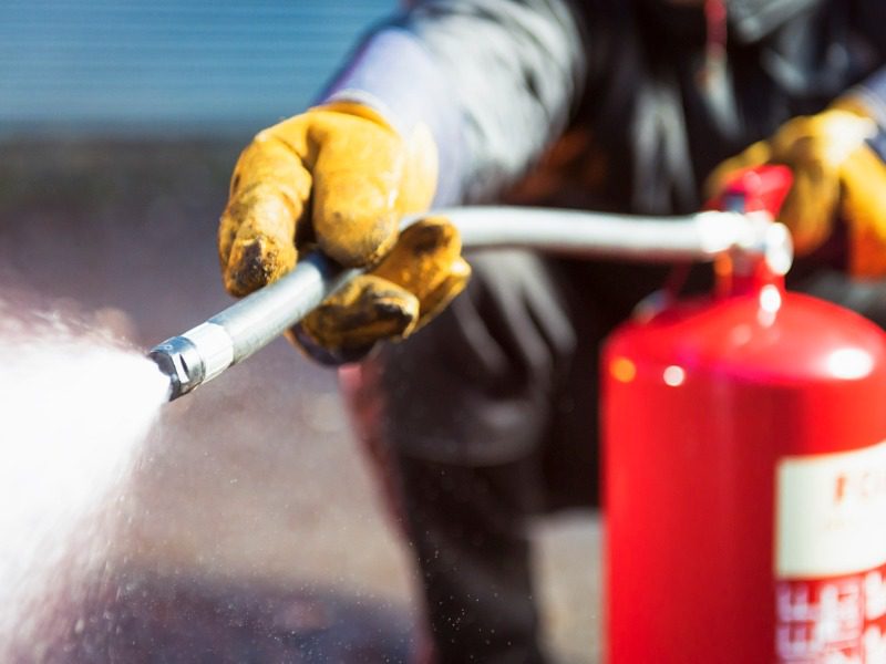 Close up of a firefighter holding and spraying firefighting foam out of an extinguisher