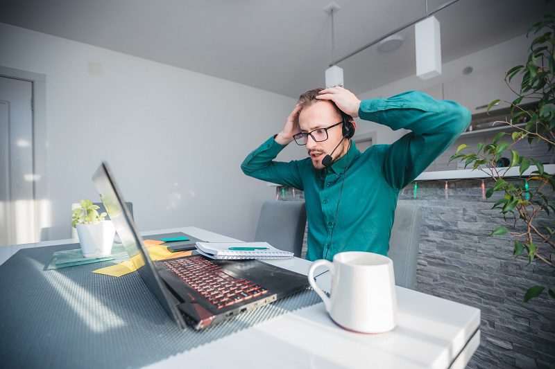 Young stressed businessman working at desk in home office shouting at laptop screen and being angry about financial situation