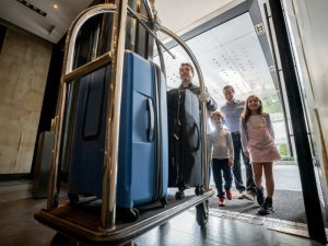 Bellhop pushing a family's luggage into a hotel lobby.