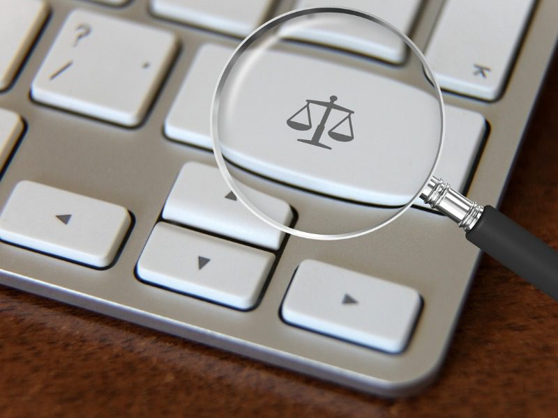 Magnifying glass over a key on a laptop keyboard which has a law scale symbol on it