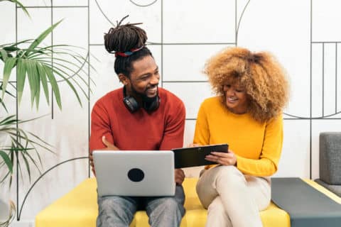 Stock photo of two african american coworkers using tablet and laptop in the office.