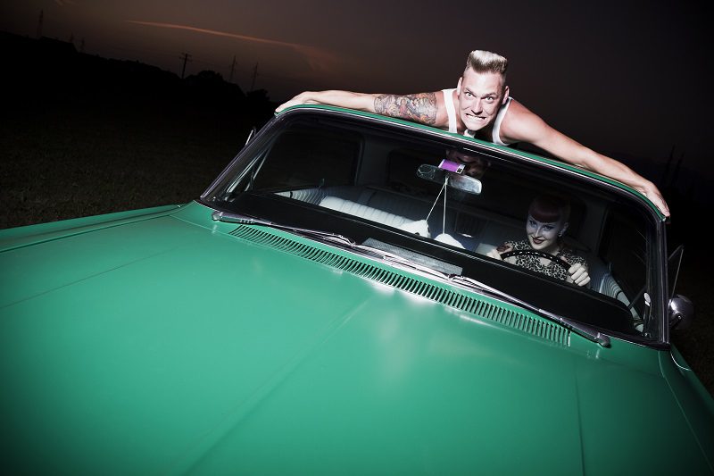 creepy rockabilly couple, girl is trying to get rid of her boyfriend who is clenching on the roof of her wildcat.