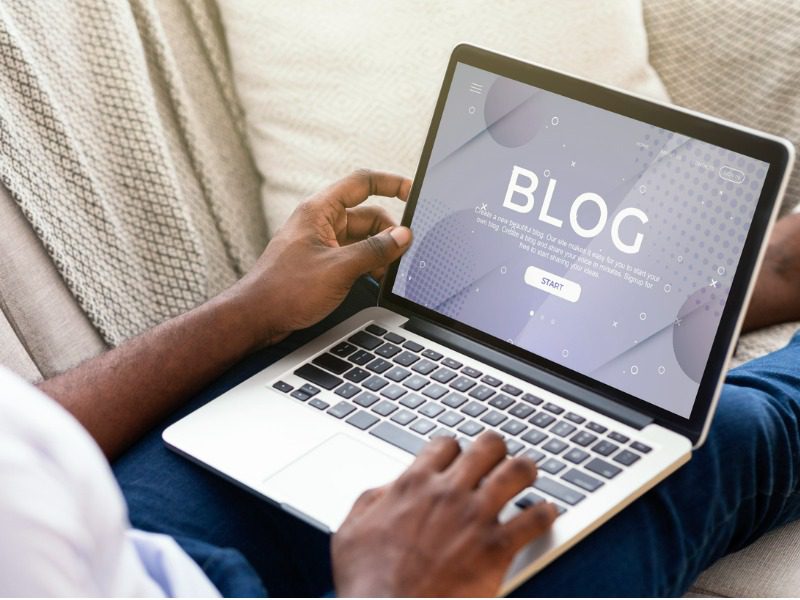 A man sits in front of his laptop with a screen that says "BLOG."