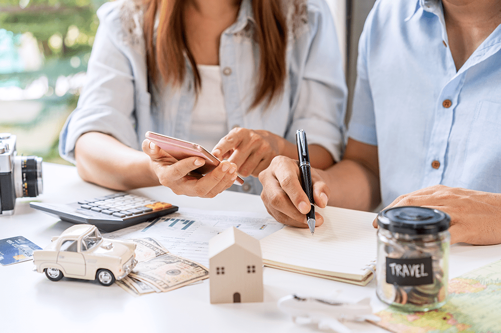 a couple sitting at a table working out their finances using a mobile phone and a calculator