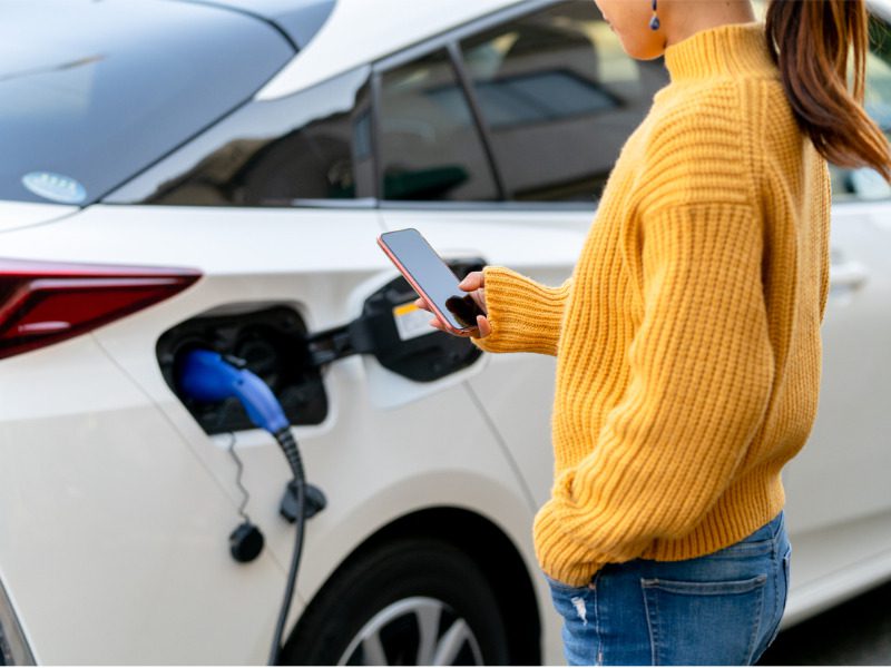 Woman using a mobile phone while charging an electric car