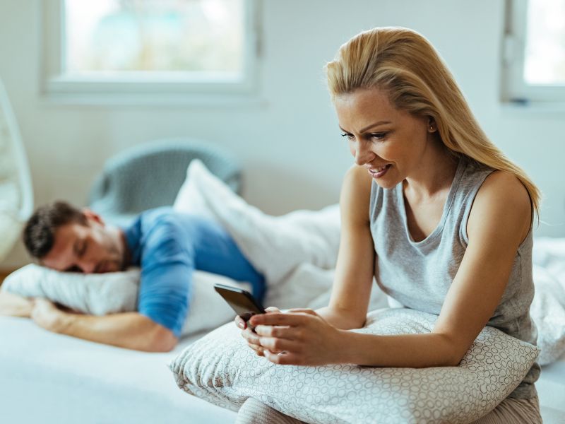 young happy woman checking her phone while sitting on the bed