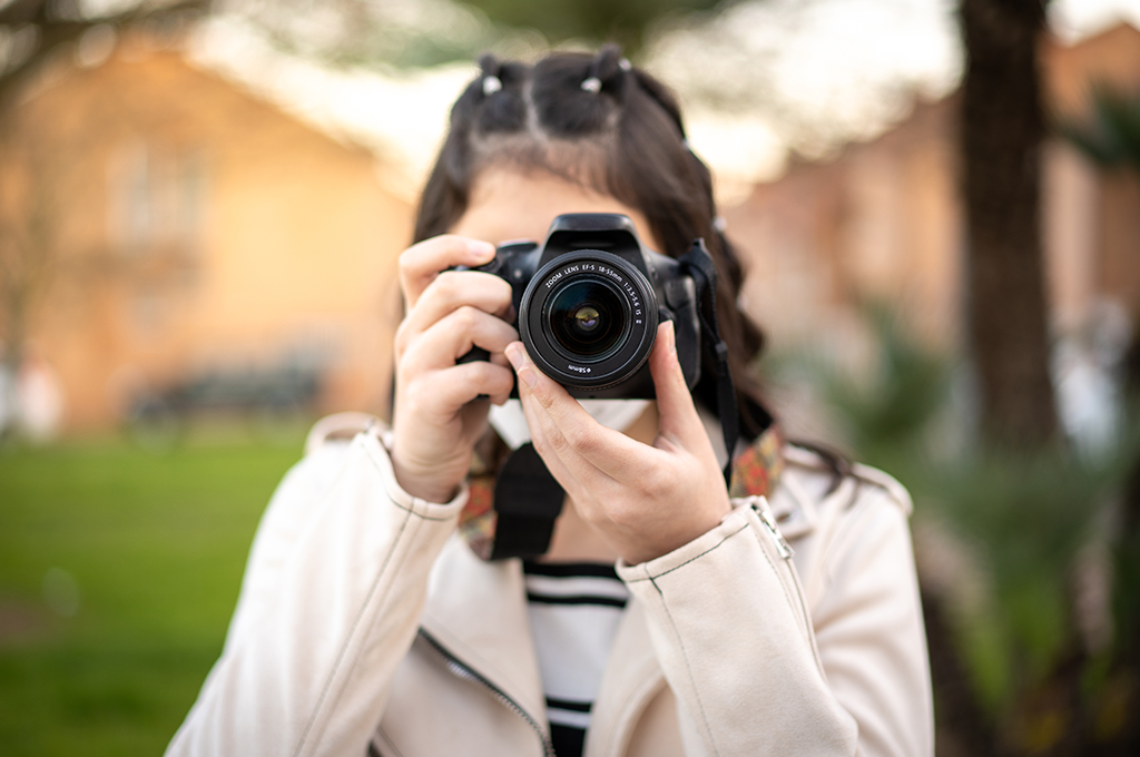 female photographer in a cream-coloured long-sleeved jacket taking a photo looking at the reader