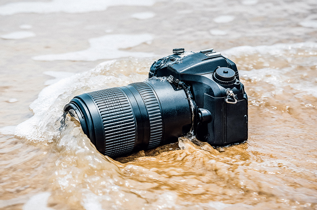 a black camera sitting on the sand with waves gently lapping over it