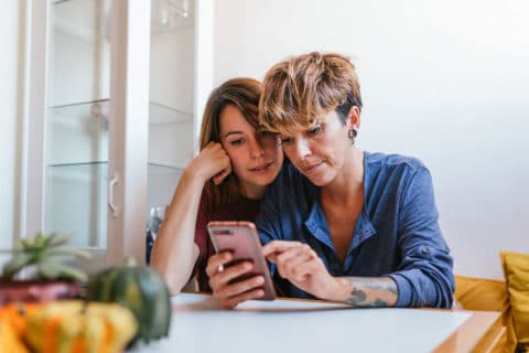 Mother and daughter sitting at the kitchen table looking at a cell phone.