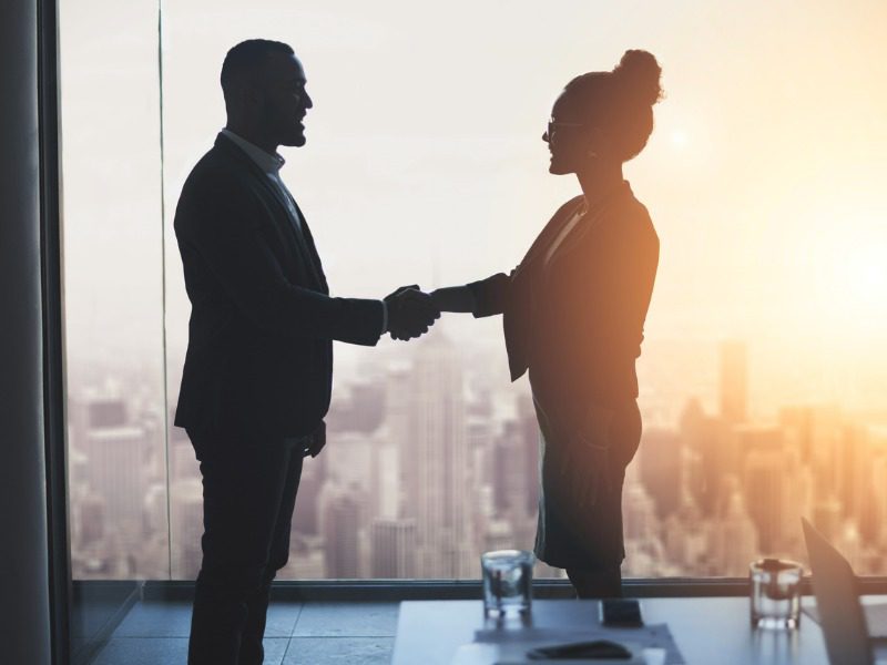 Silhouetted shot of two businesspeople shaking hands in an office