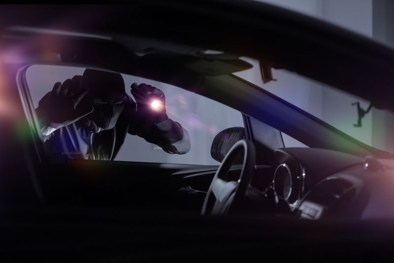 Car thief shining flashlight into the interior of a car
