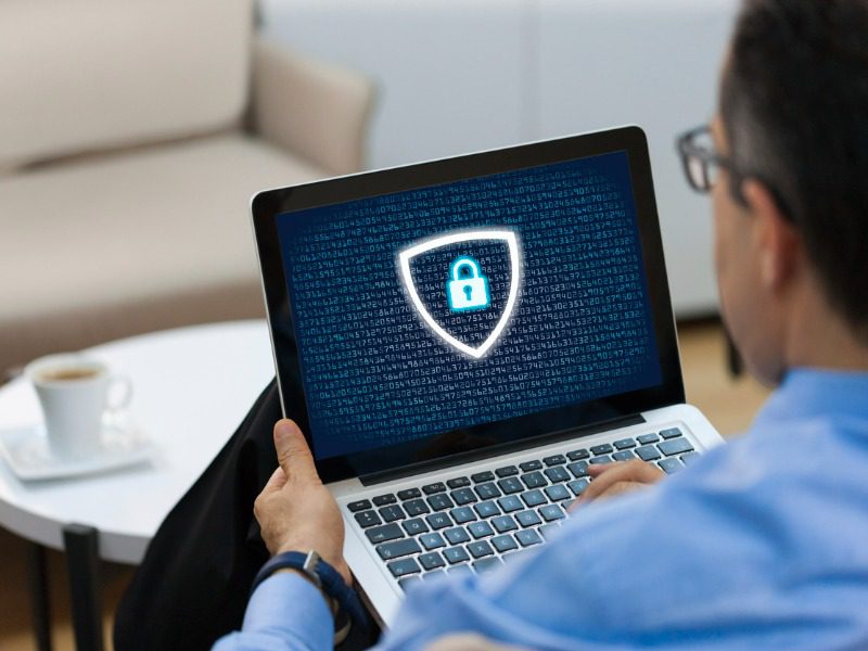 A man wearing a blue shirt sits with a laptop on his lap. On the screen is a padlock icon.