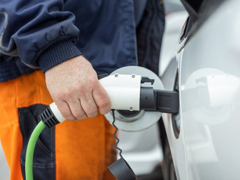 A man wearing a blue jacket and orange pants charges an electric car