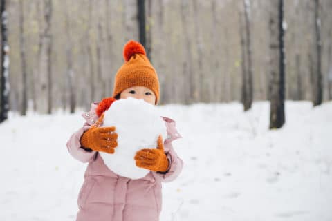 Young Asian toddle girl playing in a forest full of snow in winter.