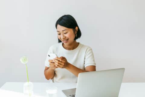 Joyful female working from home with a cell phone and laptop in a minimalist home setting