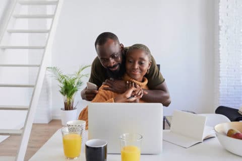 Black couple looking at a computer during breakfast time and embracing.