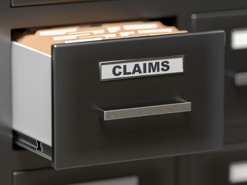 A filing cabinet drawer with a tag that says "claims" is opened and is holding stacks of brown envelopes.