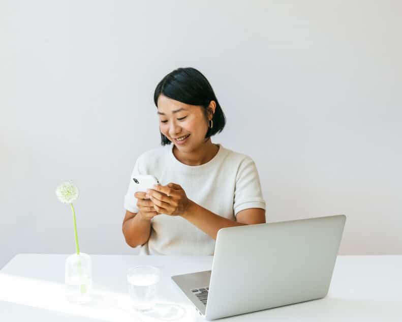 Joyful female working from home with a cell phone and laptop in a minimalist home setting