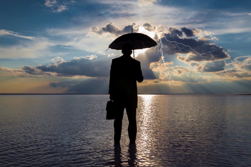 Man standing in water with an umbrella and dark clouds overhead