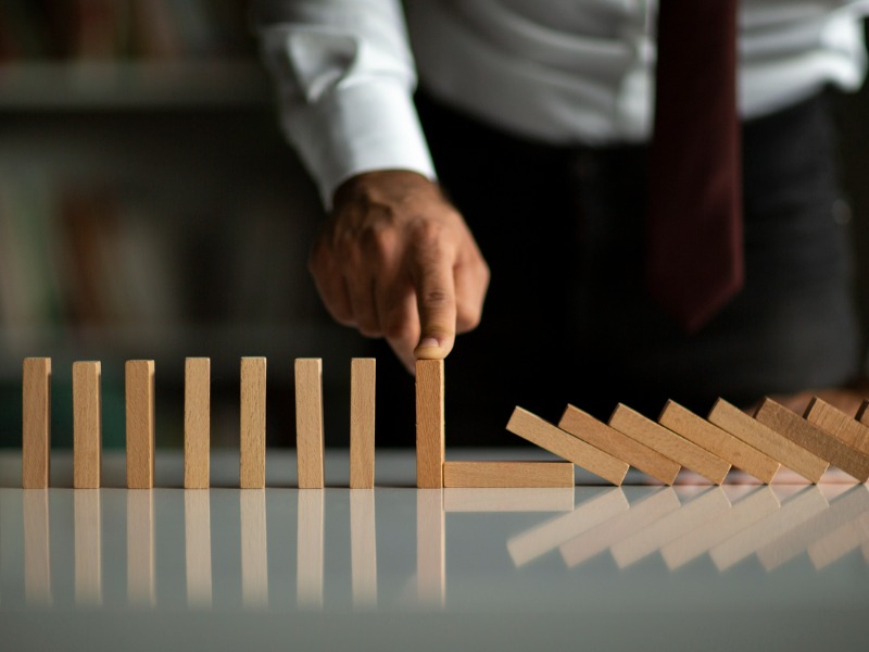 Lower shot of a businessman in a white button up shirt and red tie stopping a set of wooden dominoes with his hand