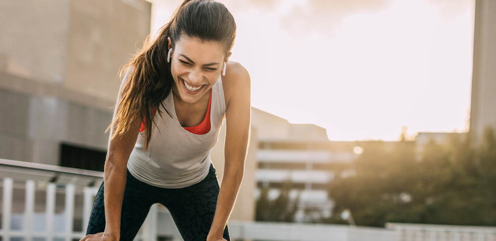 female athlete smiling and leaning on her knees after morning training session