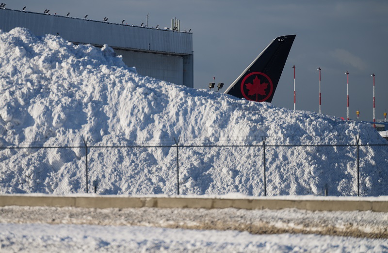 The tail of an Air Canada aircraft behind a pile of snow at Vancouver airport