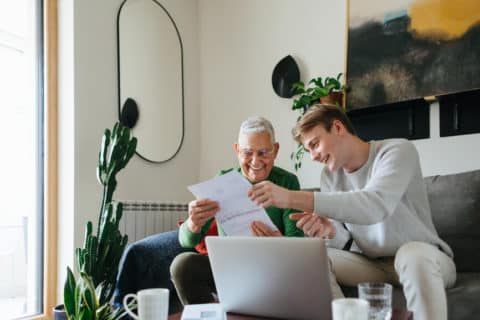 Young man and his grandfather using laptop at home, paying bills online