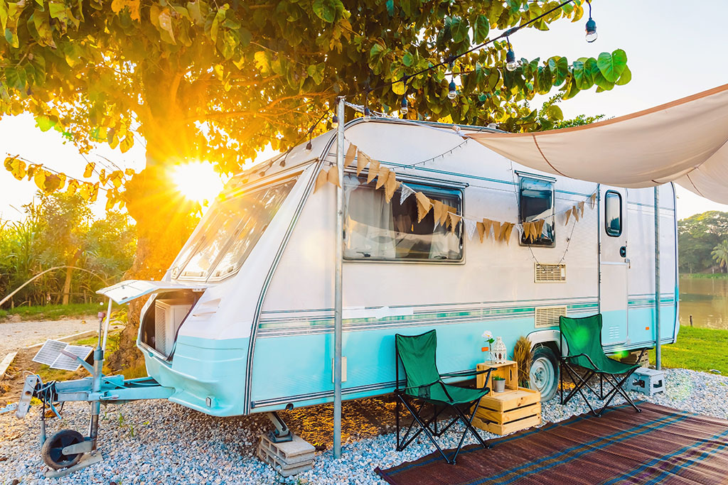 Funky exterior of a caravan with white and blue paint. Deck chairs and gazebo outside area.