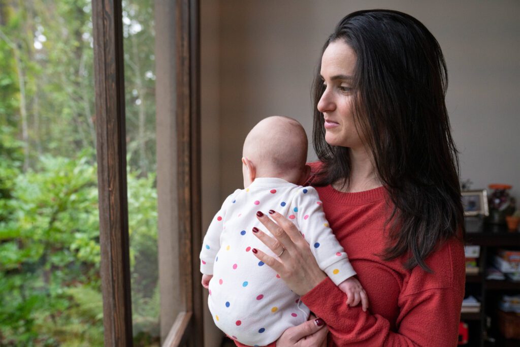 A photo shows a woman holding her infant child while facing a window.