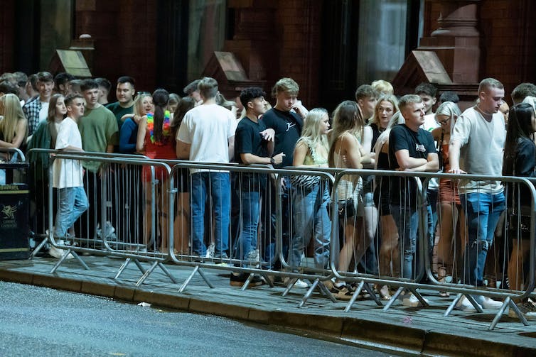 A crowd of people line up next to metal barriers. It is night time.