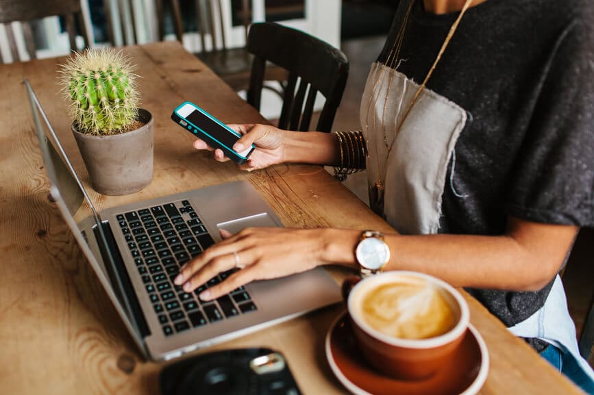 A woman at a cafe having brunch and working on her laptop and mobile phone.