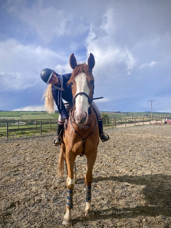 Lidija on her horse, leaning over and smiling at the camera 
