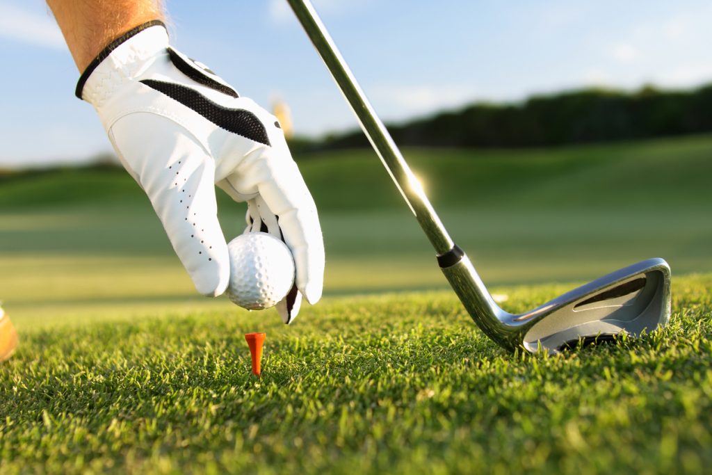 Hand wearing golf glove placing golf ball on tee next to a golf club