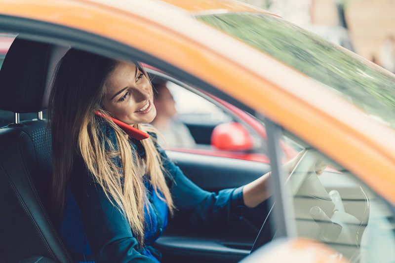 Smiling woman talking on phone while driving a car