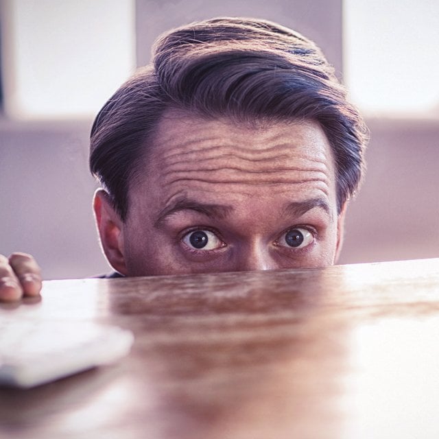 Scared man peeking over desk