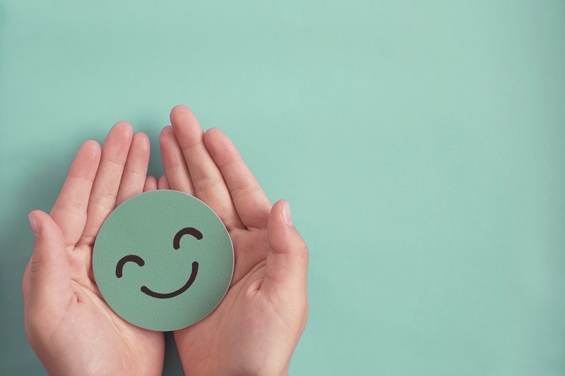 Hands holding green happy smile face paper cut, good feedback rating and positive customer review, experience, satisfaction survey ,mental health assessment, child wellness,world mental health day concept