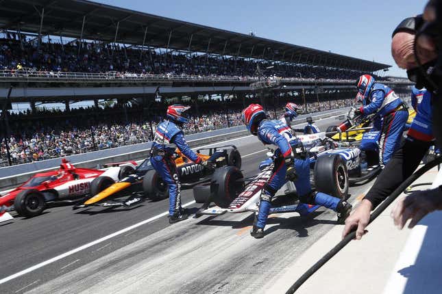 The cars of Pato O'Ward and Marcus Ericsson speed by the car of Graham Rahal as it undergoes a pit stop at the 2021 Indianapolis 500.