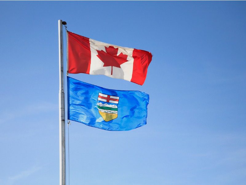 Canada flag and Alberta flag flying on a pole against blue sky