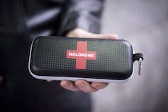 A black case about the size of a glasses case labelled with a red cross and the word Naloxone