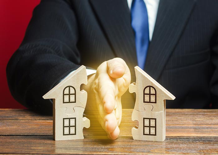 Graphic of a life insurance agent holding his hand between a little house made of jigsaw puzzle pieces, representing the ability of whole life insurance to divide assets among heirs for estate planning