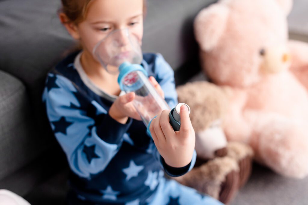 A girl uses an inhaler with a spacer attached.