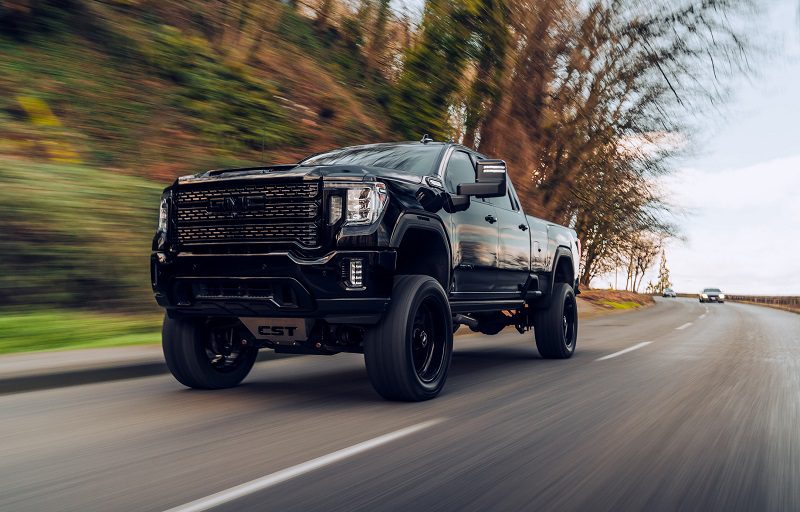 Black GMC Sierra Denali driving on the street with trees in the background