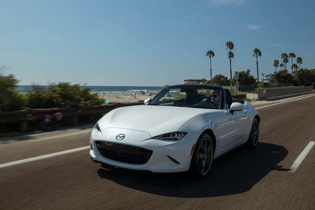 Pearl white roofless convertible 2023 mazda mx-5 miata driving on a beachside road in california