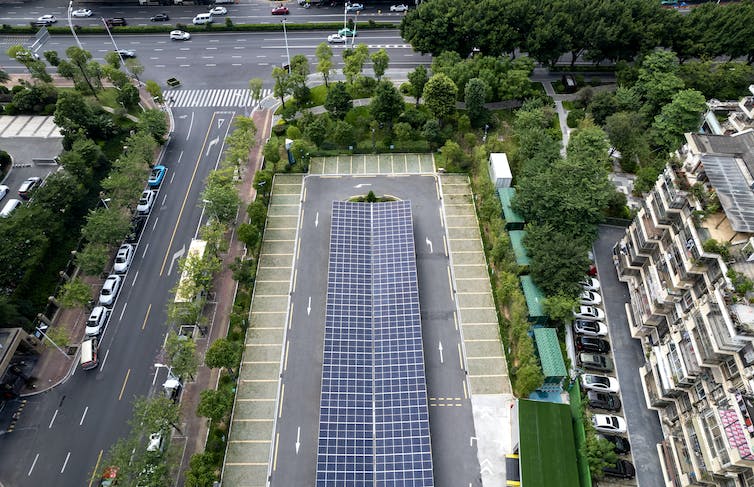 The view from high in an apartment building shows balconies below and the solar-panel covered roof over the parking area.