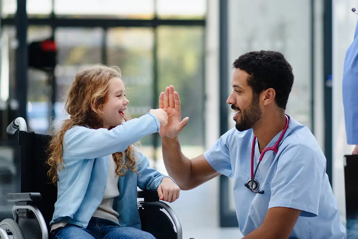 Young multiracial doctor having fun with little girl on wheelchair.