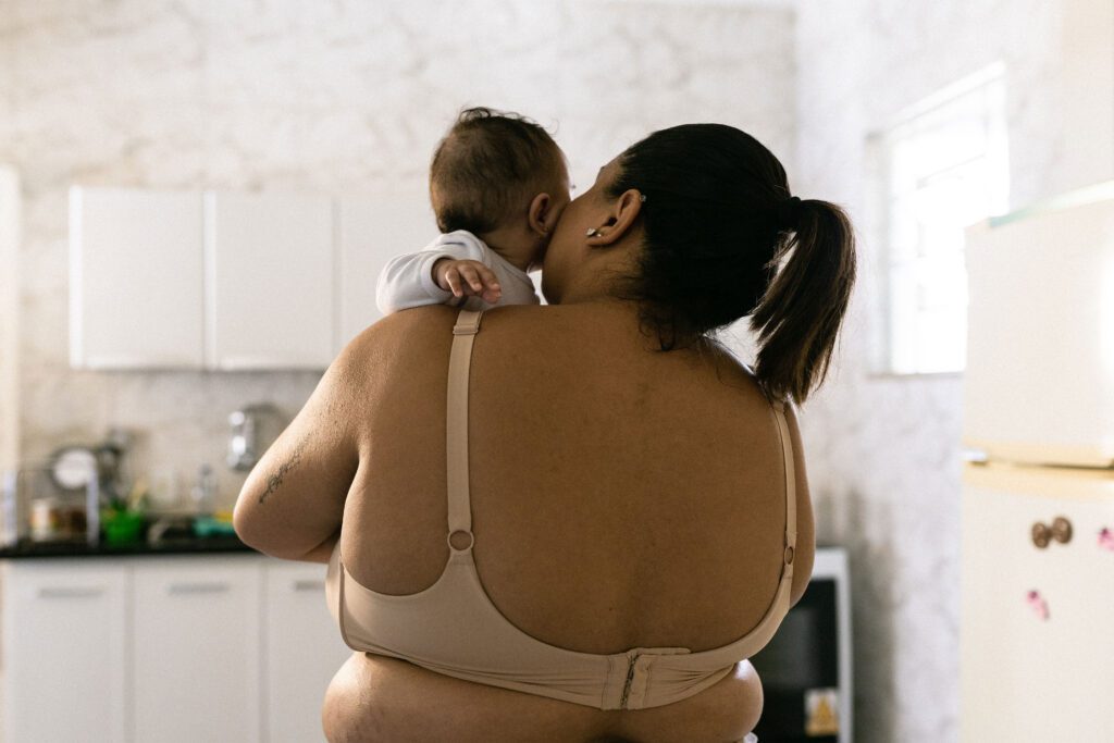 A view from behind of a woman wearing a bra and holding a baby to her cheek.