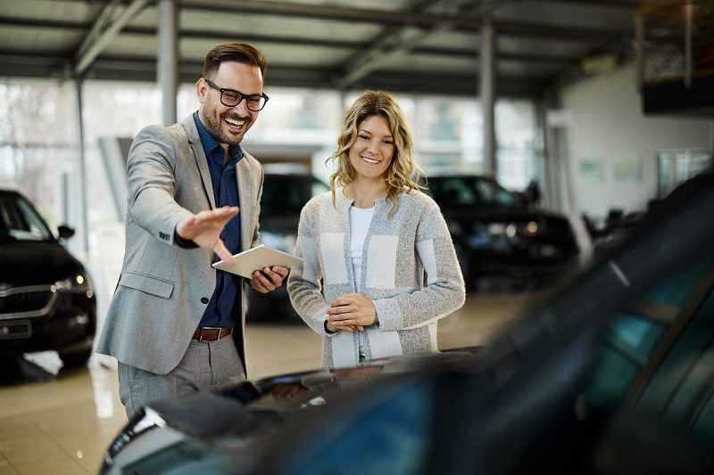 Happy car salesman showing a car to his customer in a showroom.