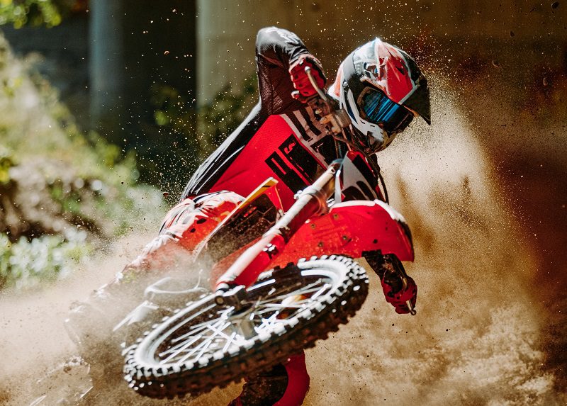 Motocross rider in red sportswear raced on dirt track in forest