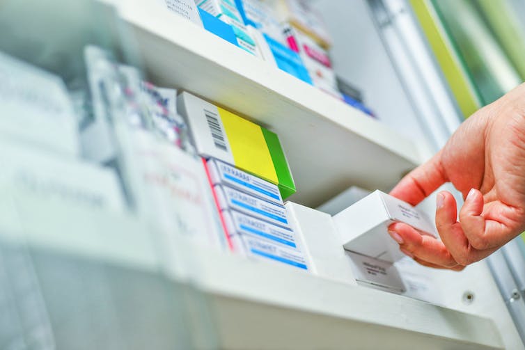 Pharmacist taking medicine box off shelf