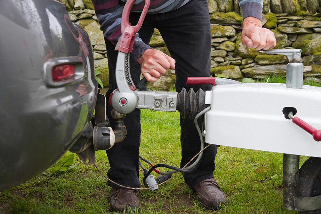 A person loading a caravan onto the back of a car 